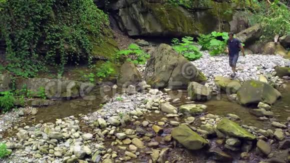 旅行者在绿色的热带森林中从石头到石头沿着一条条山河视频的预览图