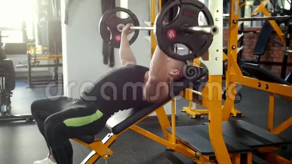 健美运动员在健身房的长凳上进行倾斜杠铃按压练习视频的预览图