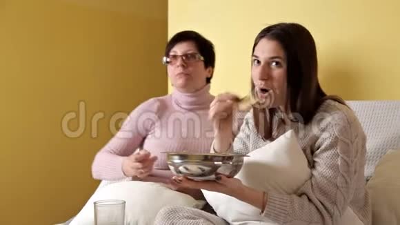 妈妈和女儿一边吃薯片一边喝电视一边喝可乐家里的舒适气氛视频的预览图