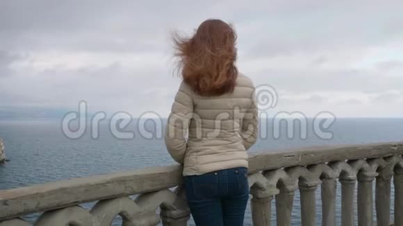 大风天站在阳台上一个长着棕色头发的瘦小女子望着大海视频的预览图