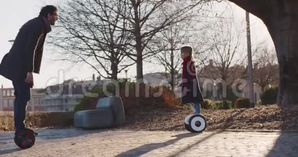 女儿亲她爸爸骑着赛格威气垫船现代未来运输技术积极的家庭公园人行道视频的预览图