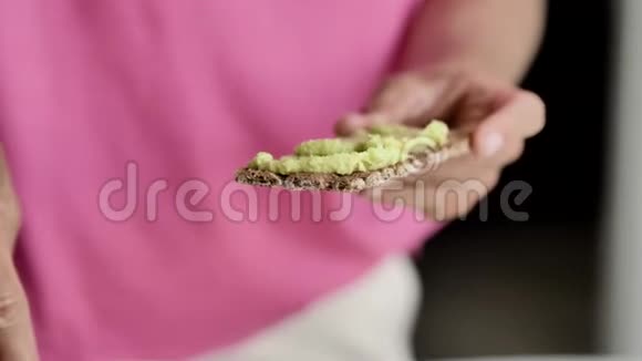 女性用手在吐司上用刀涂抹绿色膏体特写视频的预览图