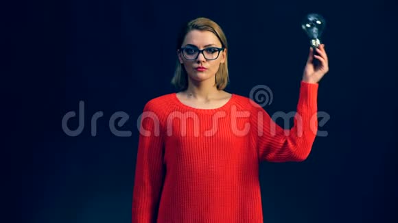 想女人戴着眼镜抬头看着手里拿着灯泡被隔离在黑色的背景上想法发现博士视频的预览图