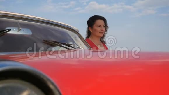 一位身穿红裙的美女正站在一辆红色老式轿车旁边视频的预览图