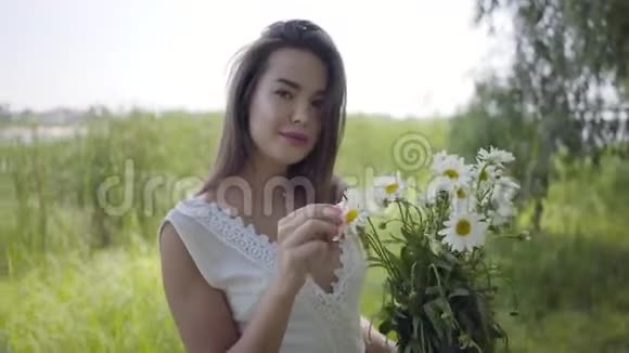 肖像可爱的年轻女孩黑发穿着一件白色的夏季时尚长裙站在田野上休闲视频的预览图