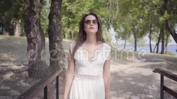肖像可爱的年轻女孩一头黑发戴着太阳镜穿着白色的夏装走在路上视频的预览图