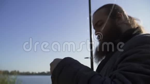 渔夫把一条虫子放在钩子上并指向它有胡子的成年男子钓鱼的肖像河流捕鱼视频的预览图