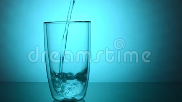 将新鲜的饮用水倒入蓝色背景的玻璃杯中视频的预览图