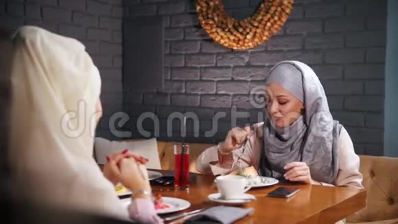 一个年轻的穆斯林妇女坐在现代咖啡馆里吃饭和说话视频的预览图