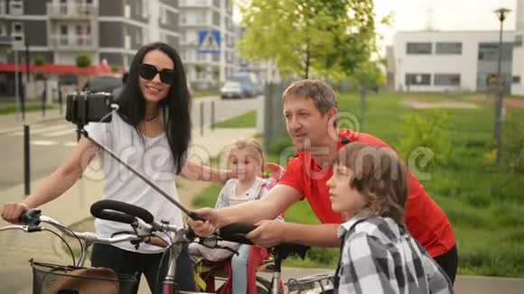 幸福的家庭在公园里带走自拍他们骑自行车后坐在自行车上父亲拿着一根自拍棒视频的预览图