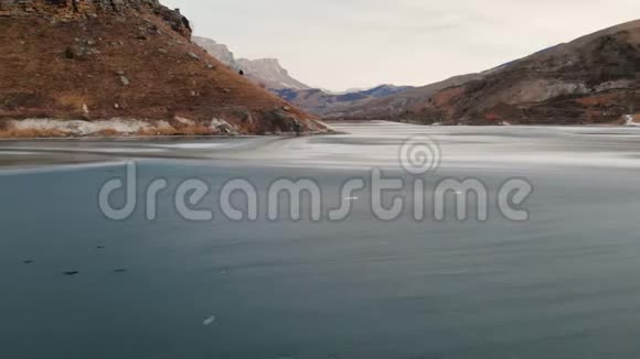 在史诗般的岩石背景下一位女摄影师沿着冰冻的山湖岸边漫步视频的预览图