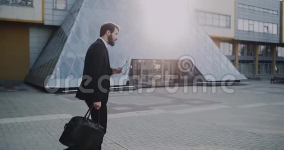 一个穿着黑色太阳镜西装走在现代商务中心的非常时髦的年轻人视频的预览图