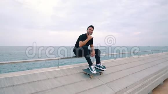 滑板运动员坐在现代城市的海露台上玩滑板视频的预览图