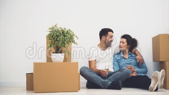 幸福的一对夫妇正坐在地板上拿着一杯白葡萄酒说话行动4K视频的预览图
