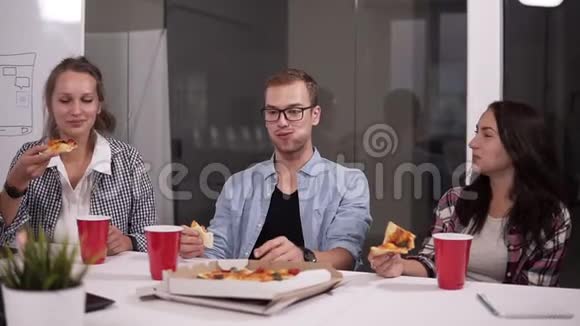 年轻的白种人同事午休时一起在办公室吃披萨笑说话玩得开心食物视频的预览图