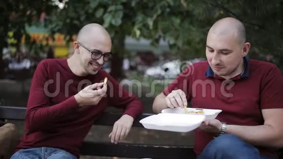 两个男人一边坐在公园的长椅上一边聊天一边在外面吃三明治视频的预览图