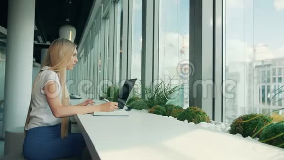 有笔记本电脑和文件的正式女人女商人一边坐在桌子旁一边用纸写字一边拿着笔记本电脑视频的预览图