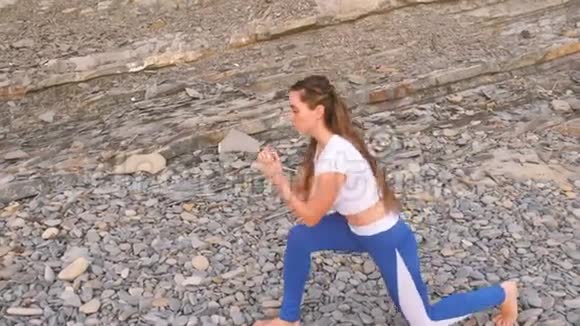 在岩石背景上做深蹲运动的女孩在呼吸练习时猛击身体视频的预览图