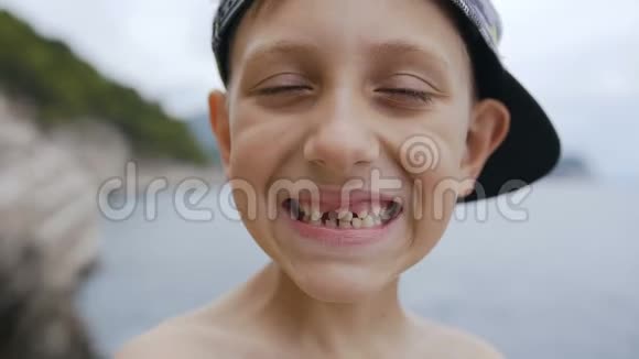 一个戴着帽子的可爱的无牙男孩正在海洋背景的摄像机上微笑微笑的学童无牙的肖像视频的预览图