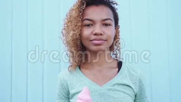 快乐的黑人女孩在蓝墙背景下缓慢移动着粉色融化的冰淇淋视频的预览图
