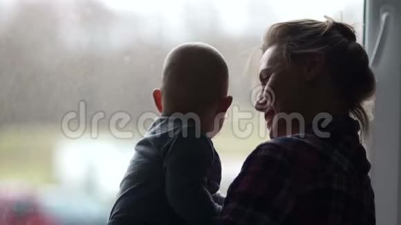 一位年轻的母亲和一个六个月大的孩子在窗户的背景下的剪影产假的家庭主妇视频的预览图