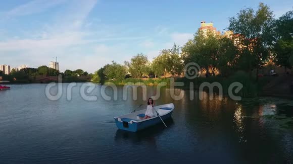 美丽的女孩坐在湖边的一艘船上挥舞着手臂视频的预览图