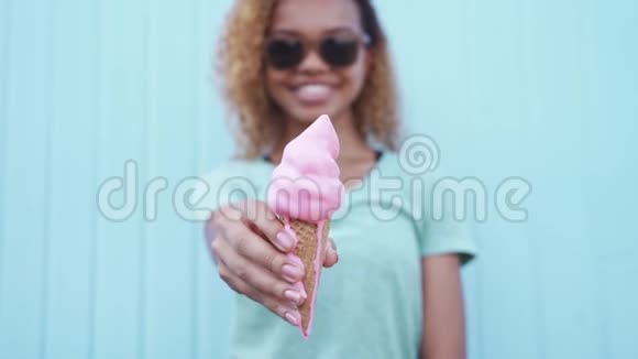 戴墨镜的快乐黑人女孩在蓝墙背景下展示了粉红色的融化冰淇淋视频的预览图