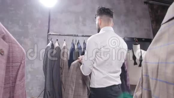 购物和时尚概念年轻的胡须男在商场或服装店挑选和试穿夹克视频的预览图