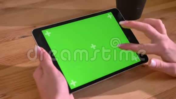 水平平板电脑的特写镜头和在木桌背景上的绿色屏幕上的手滚动视频的预览图