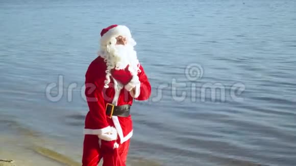 圣诞老人拿着一袋礼物站在海边或湖边视频的预览图