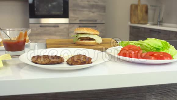 厨房的桌子上放着一个芝士汉堡上面有配料切块沙拉番茄意大利调味酱视频的预览图