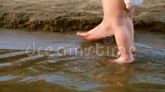 妈妈他的手牵着孩子在海滩上孩子的脚上水慢动作快关门视频的预览图