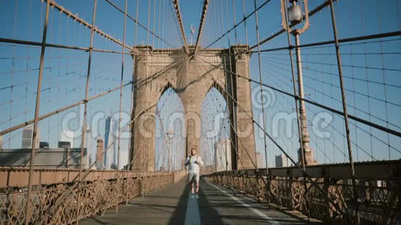 快乐的欧洲男人带着背包在阳光明媚的日子里用相机走路在布鲁克林大桥4K的上班路上环顾四周视频的预览图