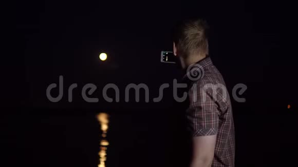 一个年轻人正在用智能手机相机拍摄一个红色的月亮视频的预览图