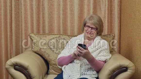 迷人的微笑女士使用智能手机在互联网上交流快乐的老妇人坐在舒适的房间里视频的预览图