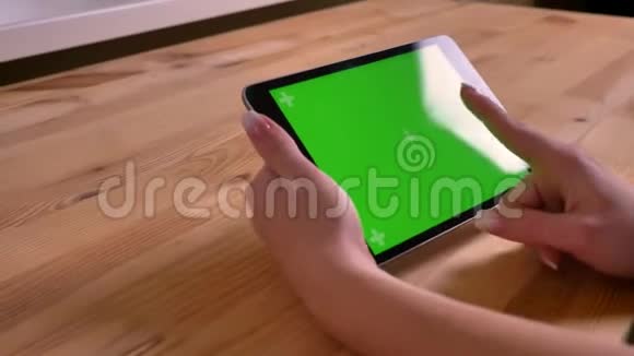 在木桌背景上的绿色屏幕上快速滑动的水平平板和女性手的特写镜头视频的预览图