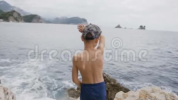 后景小男孩高高举起双手站在海面上的悬崖上海浪和岩石美丽视频的预览图