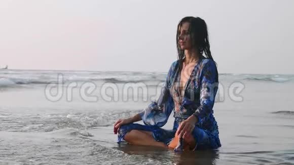 年轻的湿漉漉的女人坐在沙滩上做冥想练习视频的预览图