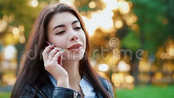 商务女性与智能手机关闭在秋季公园在日落光女孩用手机聊天视频的预览图