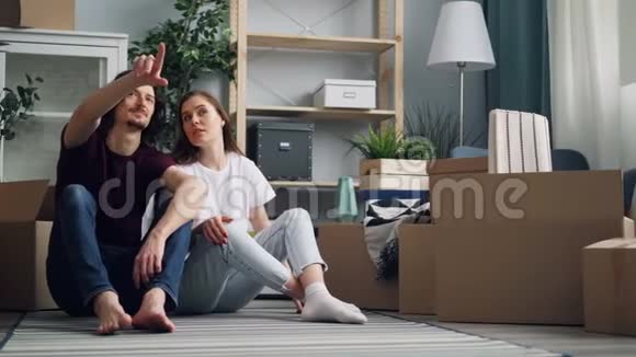 年轻夫妇坐在地板上聊天接吻盒子搬在新公寓里视频的预览图