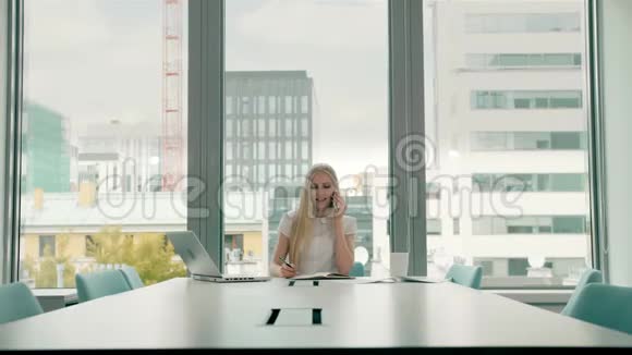 女商人在打电话时用手挥手时髦的女商人坐在桌子旁打电话视频的预览图