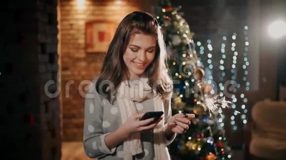 一个手里拿着火花的漂亮女孩正笑着看着圣诞节手机上的照片视频的预览图
