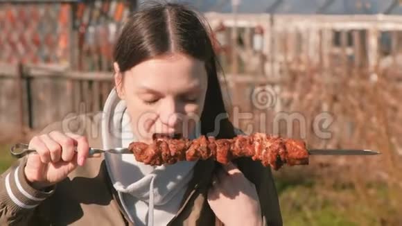 在阳光明媚的一天一个女人在后院的一个扦子上吃热肉shashlik烧烤视频的预览图