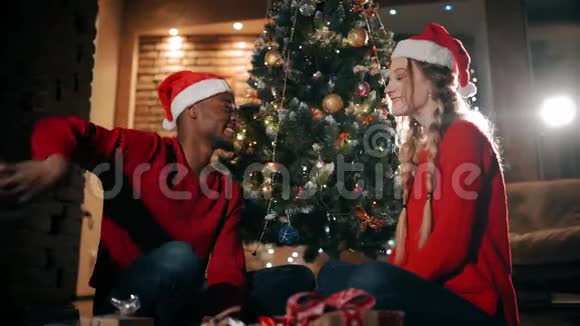 幸福的一对夫妇正坐在家里客厅的一块蓬松的地毯上一个男人正在给女孩送圣诞礼物视频的预览图