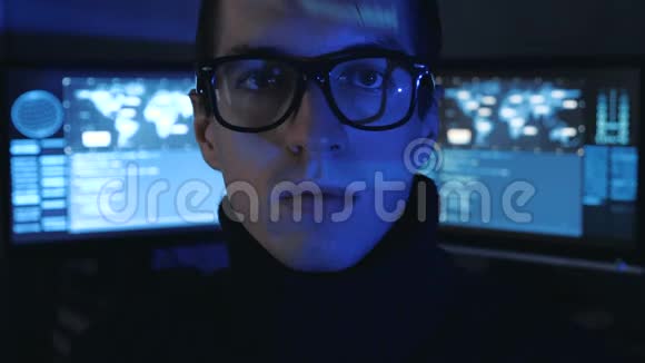 戴眼镜的Hacker程序员的肖像看着相机而蓝码字符在网络中反射他的脸视频的预览图