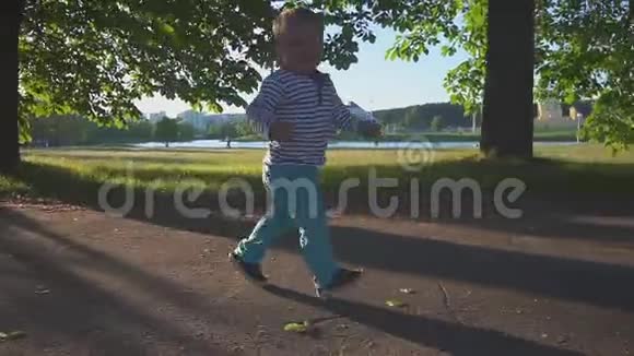 快乐的小男孩在公园和湖边的人行道上奔跑微笑着慢动作视频的预览图