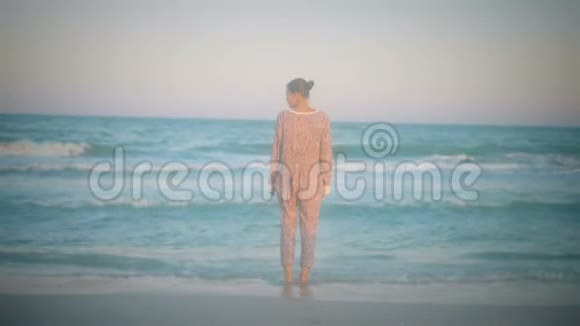 穿着睡衣微笑的女孩在浅海海岸漫步视频的预览图