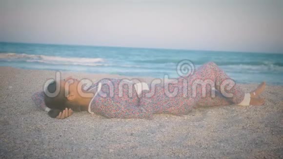 穿着睡衣的女孩躺在海滩上日落时分的海边视频的预览图