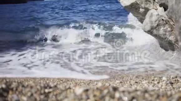 沙滩上有岩石的小波浪特写艺术美丽的蓝色波浪在沙岸和白色泡沫中破碎视频的预览图