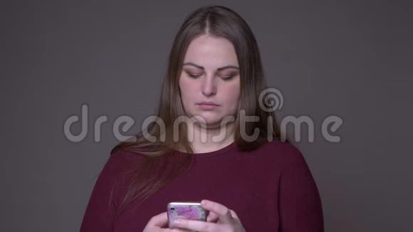 年轻超重白种人女性的特写镜头使用灰色背景的电话视频的预览图